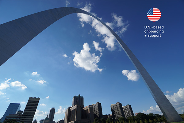 The Gateway Arch in St. Louis stands against a blue sky with clouds, accompanied by a small U.S. flag icon and the text "U.S.-based onboarding + support."