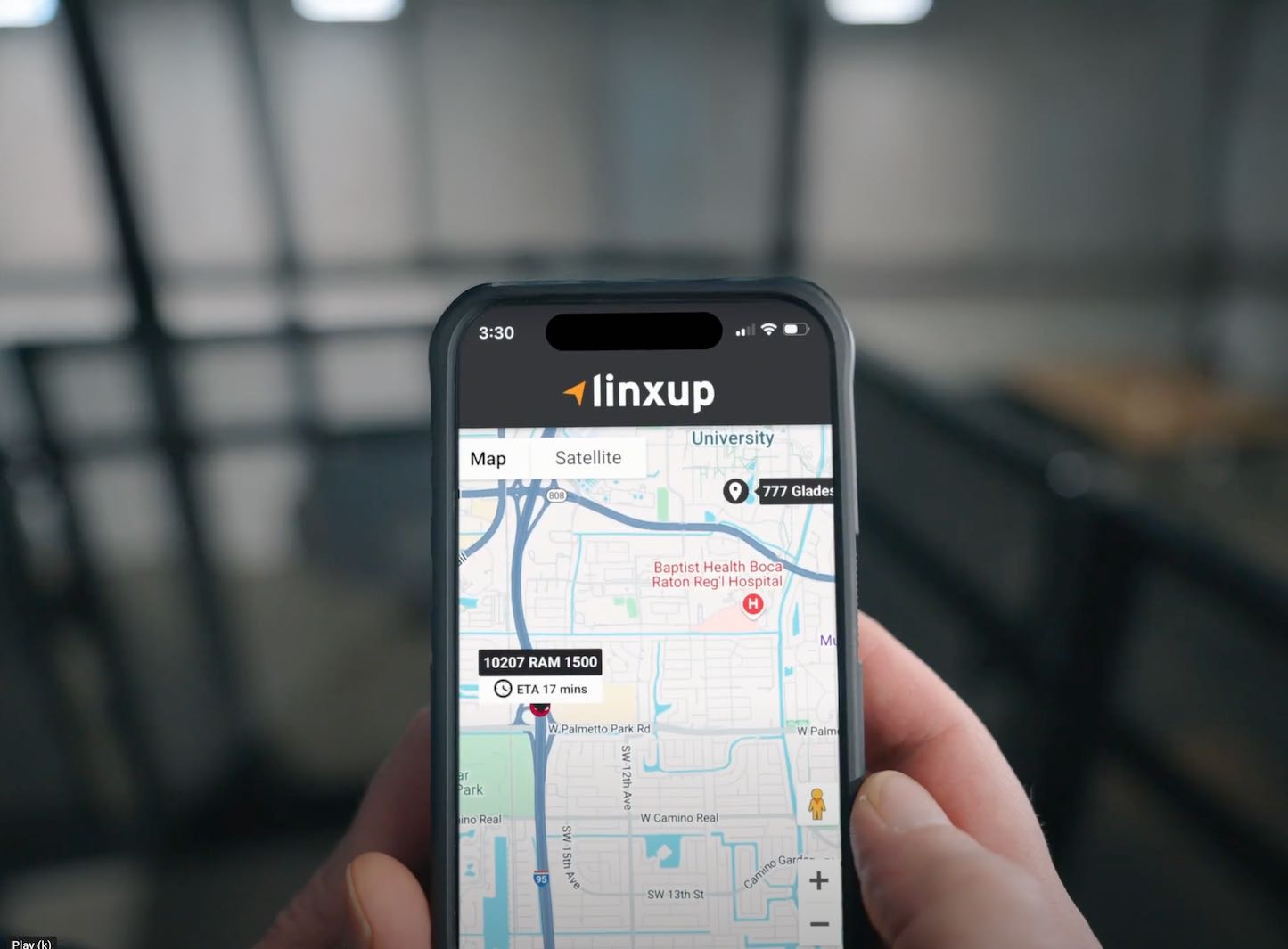 A person holds a smartphone displaying the Linxup app, which shows a live map view with a tracked vehicle location.