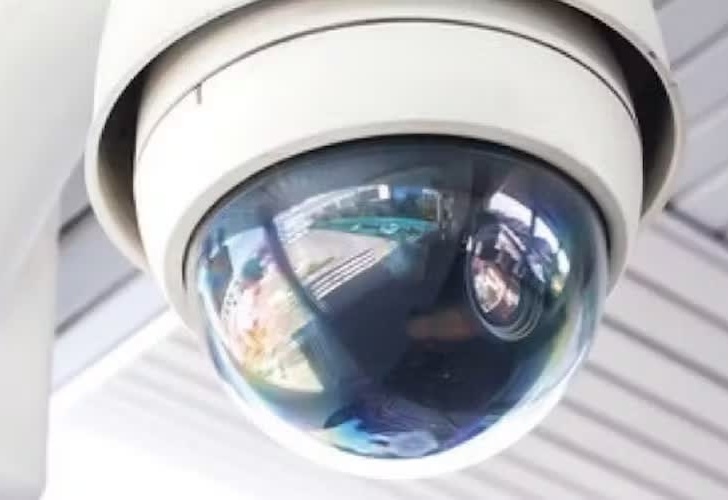 A close-up of a dome security camera mounted on a ceiling, reflecting the surrounding area.