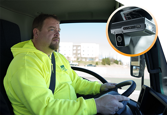 A man in a neon yellow hoodie driving a truck, with an inset circular image highlighting a dash-mounted camera.