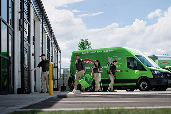 SERVPRO technicians in branded uniforms arrive at a building with their green service van to begin restoration work.