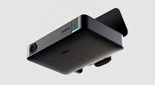 A sleek black projector with a lens on one side, featuring a minimalist design and an illuminated power indicator, is shown from a slightly angled view against a light background.
