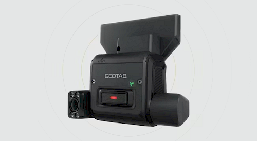 A GEOTAB dashboard camera is shown, featuring a solid black design with a lens on one side and a green indicator light above a prominent red button on the front. The camera is positioned against a light gray background.