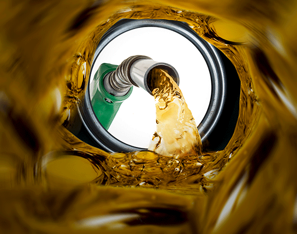 A fuel nozzle pours golden liquid into a dark opening, viewed from the perspective of inside the tank.