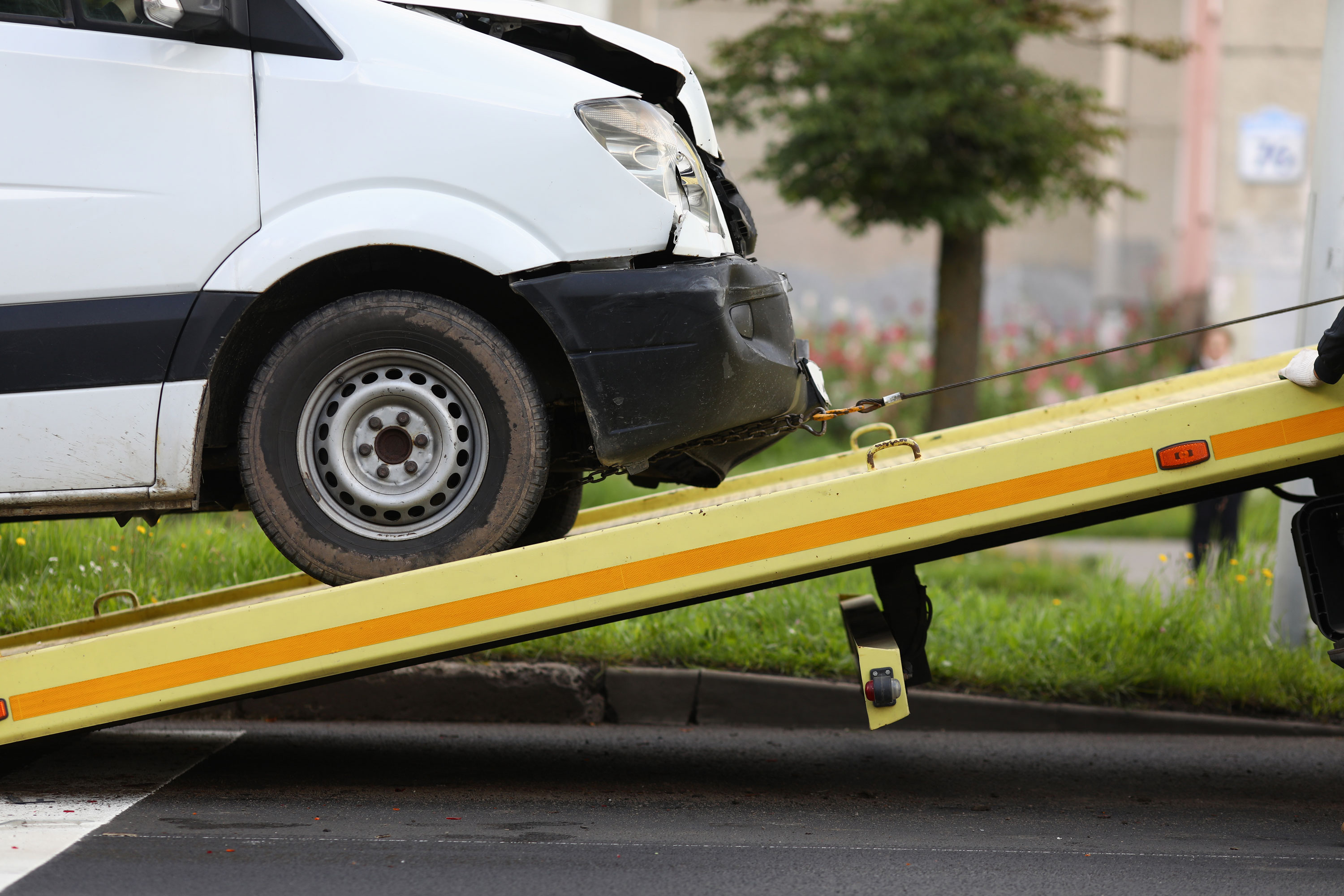A white van with visible front-end damage being winched onto the yellow bed of a tow truck.
